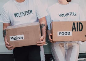 Two volunteers holding aid boxes with medicine and food labels, supporting charity causes.